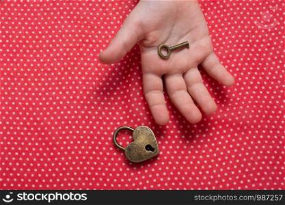 Hand holding a heart shaped lock and key on a red background