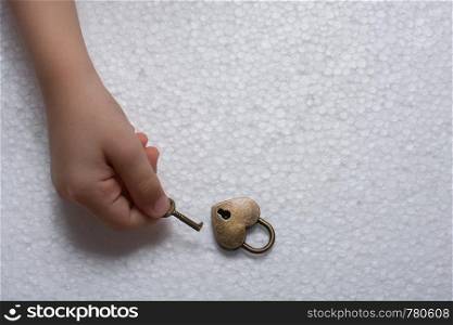 Hand holding a heart shaped lock and key on a white background