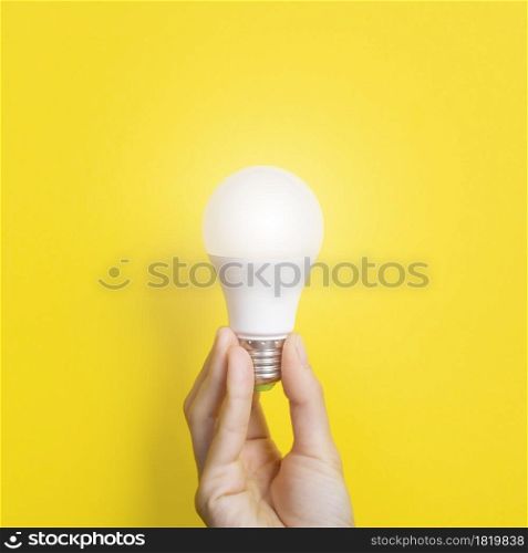 Hand holding a LED light bulb on bright yellow background. Using economical and environmentally friendly light bulb concept. Idea concept. Energy saving lamp in woman&rsquo;s hand.. Hand holding a LED light bulb on bright yellow background. Using economical and environmentally friendly light bulb concept. Idea concept. Energy saving lamp in woman&rsquo;s hand