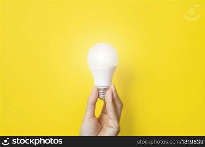 Hand holding a LED light bulb on bright yellow background. Using economical and environmentally friendly light bulb concept. Idea concept. Energy saving lamp in woman&rsquo;s hand. Banner with copy space.. Hand holding a LED light bulb on bright yellow background. Using economical and environmentally friendly light bulb concept. Idea concept. Energy saving lamp in woman&rsquo;s hand. Banner with copy space