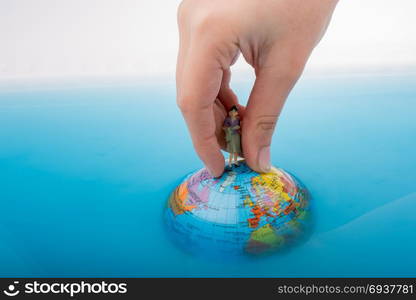 Hand holding a little figurine on the top of the globe in water