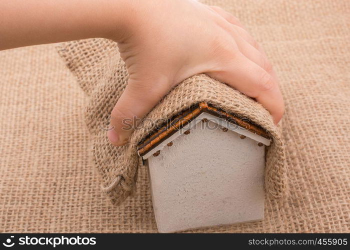 Hand holding a little model house on and under a canvas