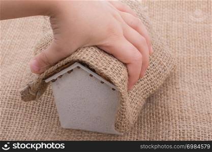 Hand holding a little model house on and under a canvas
