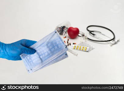 Hand holding a medical mask against the background of a stethoscope and tablets. Coronavirus Protection Concept. medical cotton mask