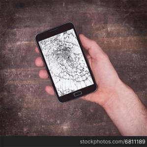Hand holding a mobile phone with a broken screen, white display