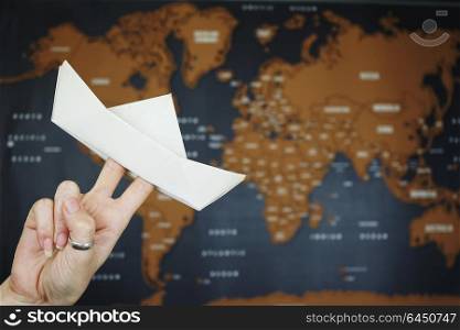 Hand holding a paper boat against a map of the world