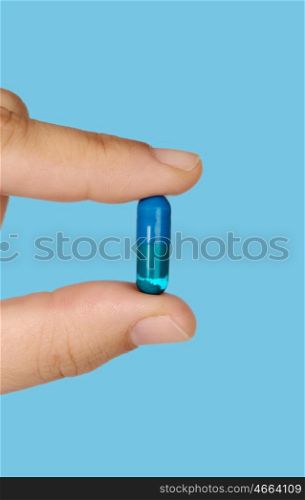 Hand holding a pill medication on blue background