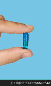 Hand holding a pill medication on blue background