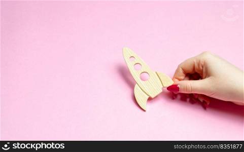 Hand holding a rocket on a pink background. Concept of startup or crowdfunding. Popularization of popular science and technology, passion for rockets and space travels. development of space tourism