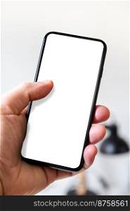 Hand holding a smartphone with blank white screen. White office background.. Hand holding a smartphone with blank white screen. Office background.