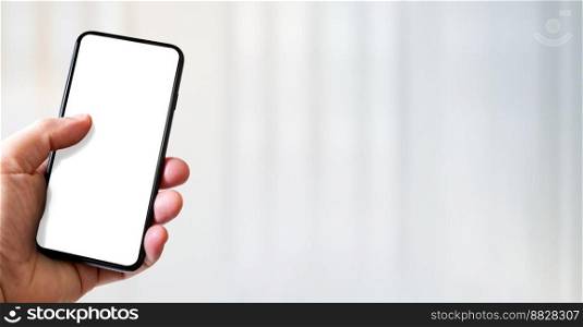 Hand holding a smartphone with blank white screen. White office background. Horizontal banner.. Hand holding a smartphone with blank white screen. Office background. Horizontal banner.