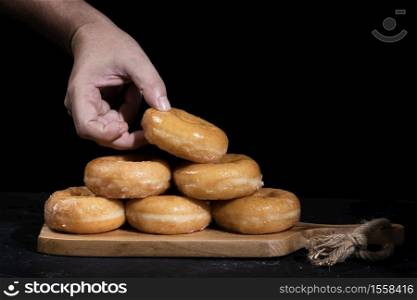 hand holding a sugar doughnut from a mountain on a wooden board with a black background