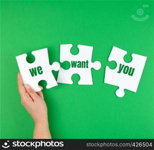 hand holding a white puzzle with the words we want you, green background