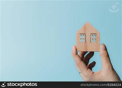 Hand holding a wooden house model on blue background for housing and property concept