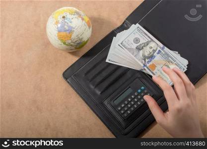 Hand holding American dollar banknotes beside a globe