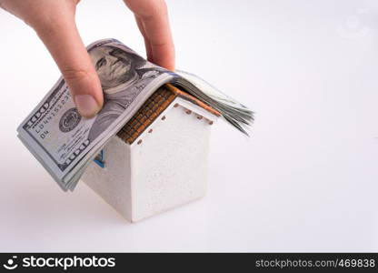 Hand holding American dollar banknotes on the roof of a model house on white background