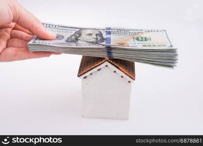 Hand holding American dollar banknotes on the roof of a model house on white background