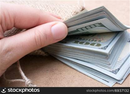 Hand holding banknote bundle of US dollar on a linen canvas background