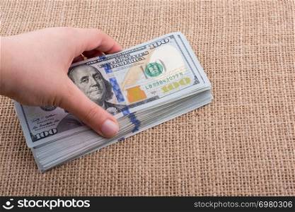 Hand holding banknote bundle of US dollar on a linen canvas background
