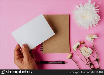 Hand holding blank card, notebook, pen and flower on pink background