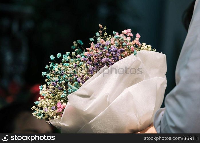 Hand holding bouquet of dried gypsophila flowers wrapped in paper 