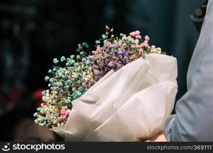 Hand holding bouquet of dried gypsophila flowers wrapped in paper 
