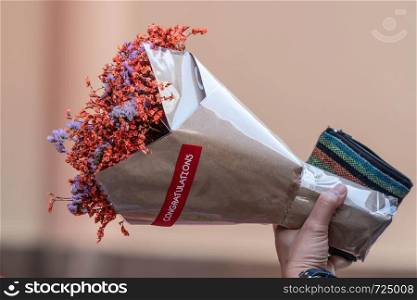 Hand holding bouquet of dried orange flowers wrapped in paper