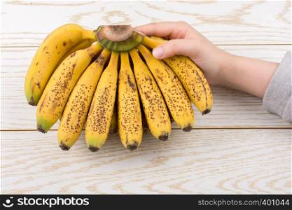 Hand holding bunch of freckled bananas on a wooden texture