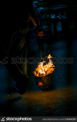 Hand holding burning charcoal oven for cooking with flame and fire spark on dark background