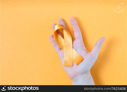 Hand holding Childhood Cancer Awareness Yellow Ribbon and stethoscope on yellow background with copy space. Childhood Cancer Day February, 15. Childhood Cancer Awareness concept
