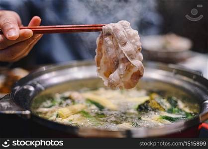 Hand holding chopsticks with ripe Kurobuta Pork in Shabu Shabu and Sukiyaki hot pot. Food concept with gourmet Japanese hot pot cuisine.