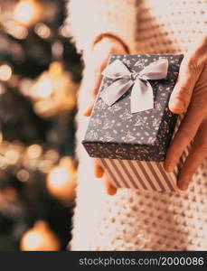 hand holding Christmas gift box in front of holiday lights