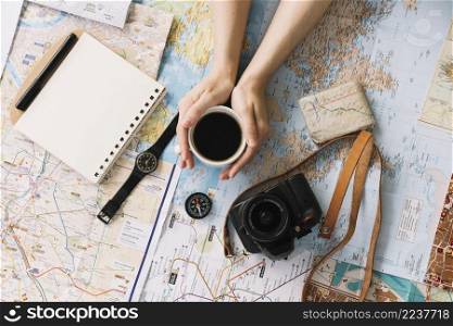 hand holding coffee cup map surrounded with spiral notepad compass wristwatch camera strap