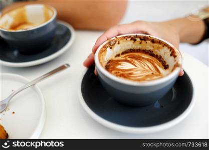 Hand holding coffee cup on white table at cafe background, top view, food and drink concept