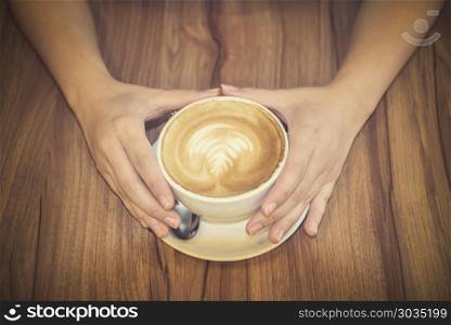 Hand holding coffee cup on wood table.