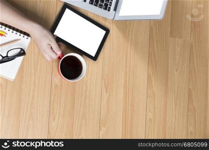 hand holding coffee cup with tablet and computer notebook on office desk