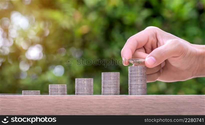 Hand holding coin and stack of money on wood table. Pension fund concept.