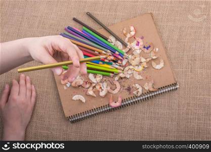Hand holding Color Pencil over a notebook with pencil shavings