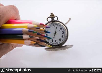 Hand holding Color Pencils beside a pocket watch on a white background