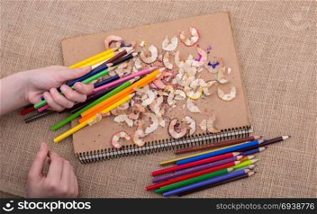 Hand holding Color Pencils over a notebook with pencil shavings