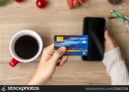 Hand holding credit card for online shopping on smartphone during drinking coffee. Merry Christmas eve, December, seasonal, Black Friday sale, New Year and holiday concept