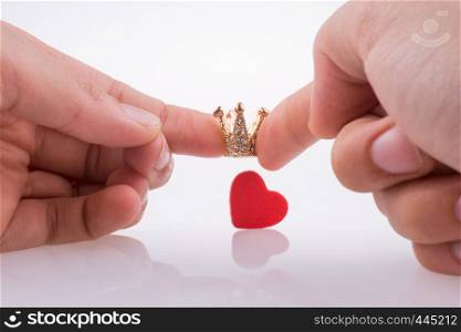 Hand holding crown near a red heart on a white background