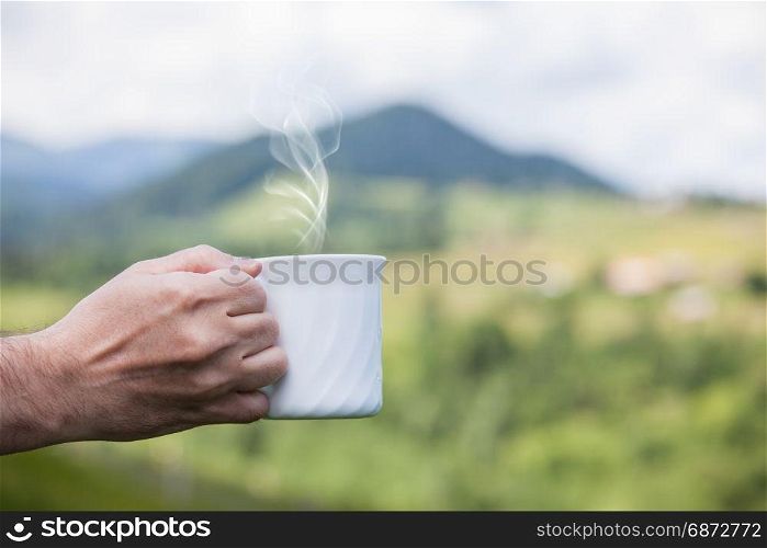 Hand holding cup of coffee over nature outdoor background