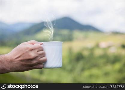Hand holding cup of coffee over nature outdoor background