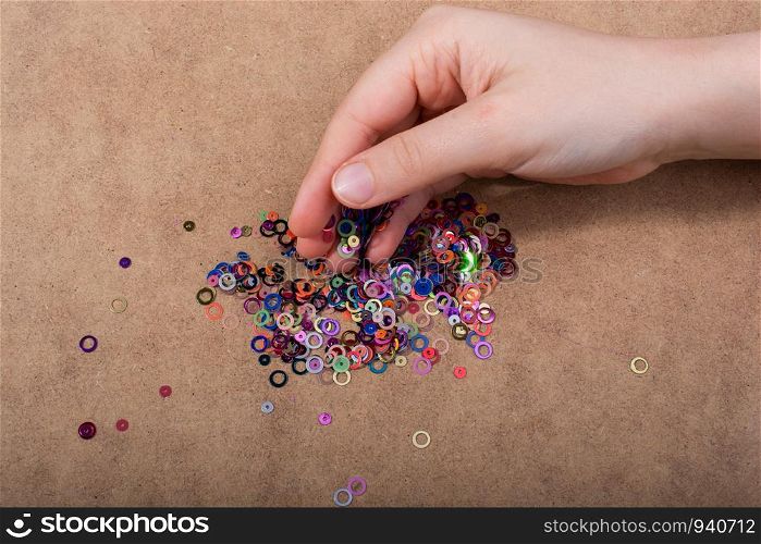 Hand holding decorative shiny colorful confetti on a wooden background