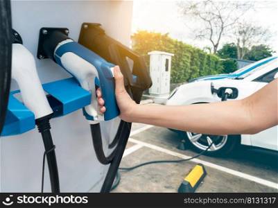 Hand holding electric plug-in charger on blur car charging. EV car charging at electric car charging station. EV car charging point. Electric vehicle fast charge. Sustainable power. Green energy.