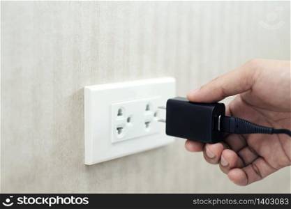 Hand holding electric plug into Electricity Socket on clean cement wall