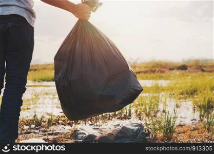 hand holding garbage black bag at river for cleaning with sunset