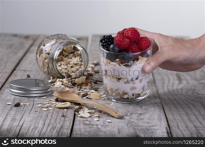 hand holding glass of cereal with yogurt and fruits of the forest, healthy breakfast concept