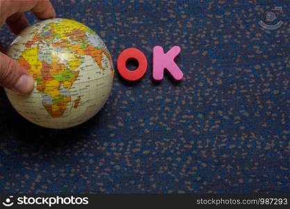 Hand holding globe model beside word OK